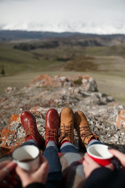 Closeup of hands with mugs and feet against background of mountains Firstperson view