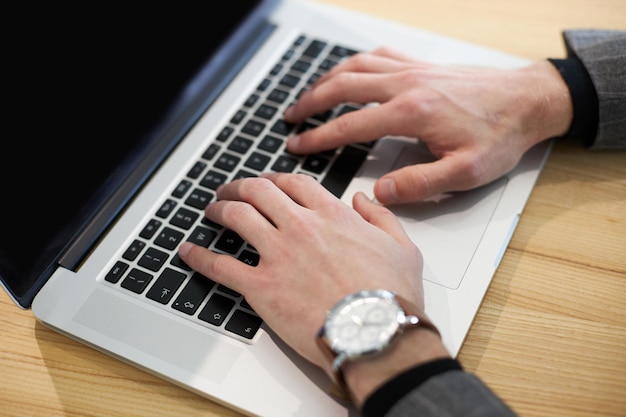 Closeup of the hands with stylish wrist watch of businessman on laptop keyboard during online work