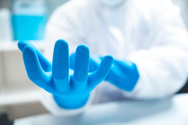 Closeup of hands of a young unrecognizable scientist, researcher and doctor wearing blue hand gloves with white PPE kit and uniform with covid-19 face protection mask for safety in laboratory