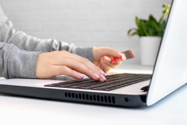 Photo closeup of hands of a young woman holding credit card and using a laptop