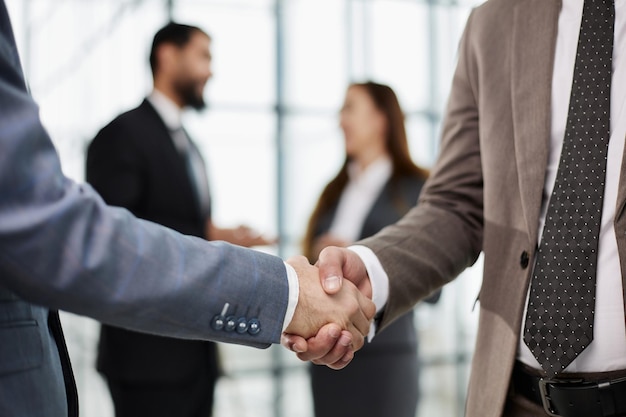 Крупный план рукопожатия деловых партнеров на фоне коллег