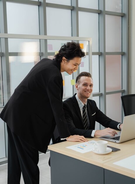 Closeup handsome Caucasian businessman smile and looking at camera happy working with businesswoman using laptop. positive mood working together with partnership. colleague relationship in office.