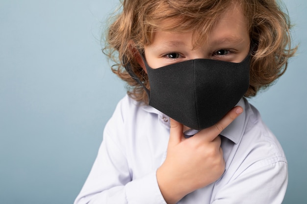 Closeup handsome curly blonde little boy in medical black mask standing