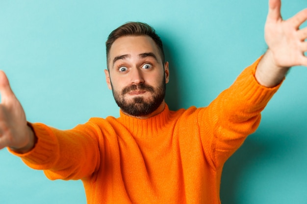 Closeup of handsome happy man reaching hands forward stretching arms for hug standing against turquo...