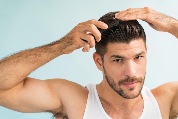 Primo piano del bel maschio che si pettina e si acconcia i capelli castani mentre si guarda negli occhi in studio