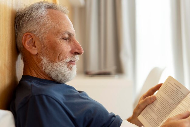 Крупным планом красивый серьезный пожилой мужчина читает книгу, лежа в постели утренней рутины Привлекательный успешный дедушка отдыхает в гостиной Концепция релаксации