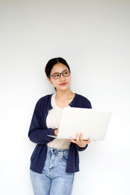 アジアの若い女性学生がカジュアルな服を着て白いグラディエントの背景にラップトップをタイピングしている