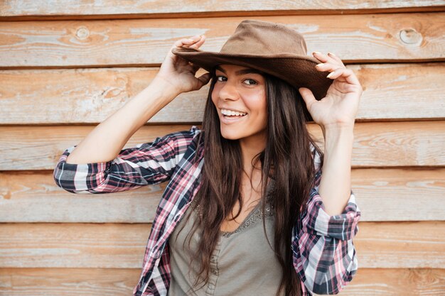 Closeup of happy beautiful young woman cowgirl in hat over wooden background