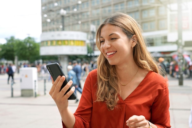 Primo piano della donna casual felice che guarda lo schermo dello smartphone in piazza alexanderplatz a berlino germania