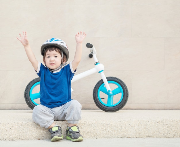 Closeup happy kid sit and hand up with bicycle on stone wall background