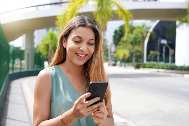 Closeup of happy woman in city using OVP or social media platform on smartphone
