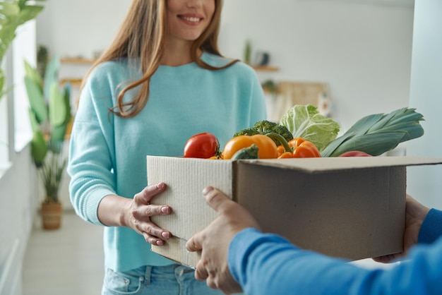 Primo piano della giovane donna felice che accetta scatola con generi alimentari dal fattorino a casa