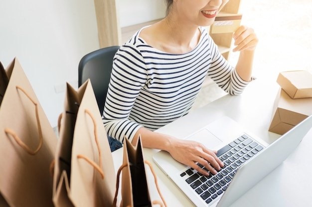 Closeup of happy young woman holding credit card inputting card information while and using laptop computer at home. Online shopping concept.