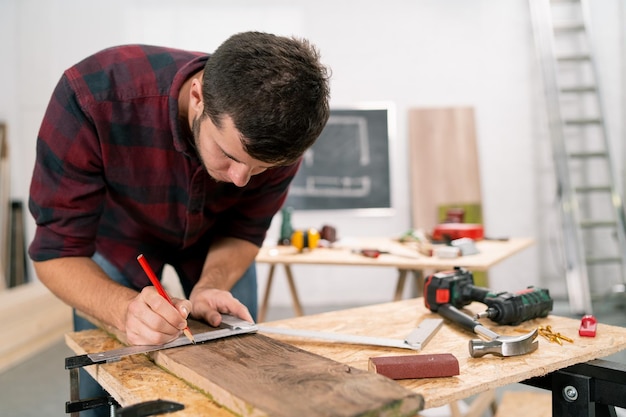 Closeup of a hardworking professional carpenter holding a angular ruler and pencil while measuring a