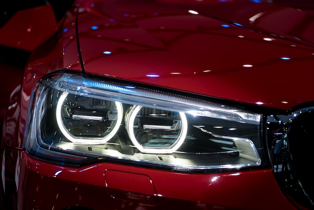 Photo closeup headlights of modern red car during turn on light in night.