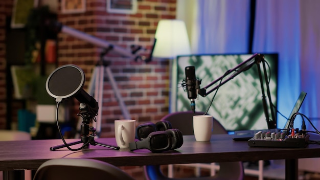 Closeup of headphones and professional microphone on empty vlogger desk ready for live talk show broadcast on internet. Detail of equipment for dual vlog on empty desk for online podcast streaming.