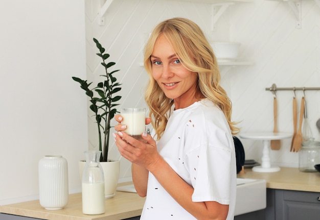 Closeup on of a healthy woman with a glass of milk in her hands in the kitchen.