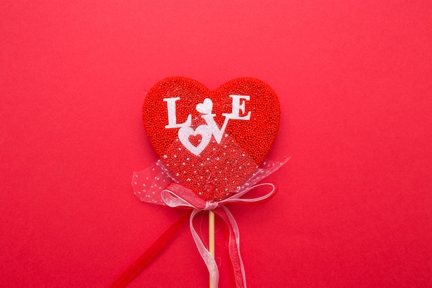 Closeup of a heart with a decor on a stick on a red isolated background. Spell love in white letters.