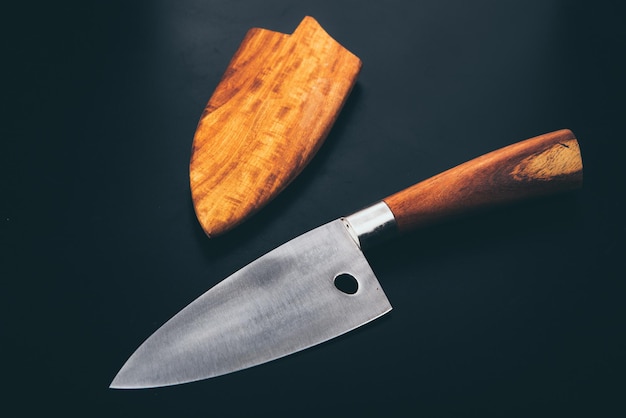 Closeup high-angle view of open stainless steel professional chef knife with wooden cover on side isolated on black background