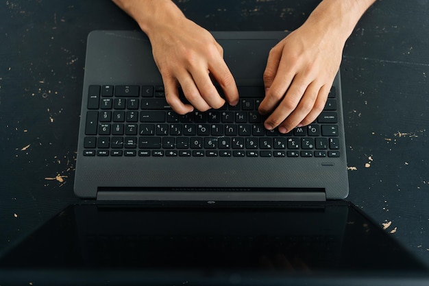 Closeup high angle view of unrecognizable business man typing\
texting on modern laptop keyboard male employee sitting at black\
desk working on computer