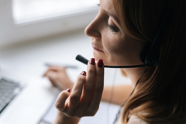 Photo closeup highangle view of female operator talking using headset and consulting client sitting at window sill with laptop from home office