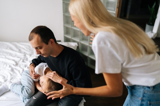 Closeup highangle view of scared father and daughter hugging each other sitting on bed while aggressive mother angrily yelling at them at home