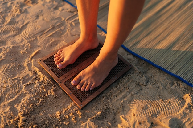 Closeup highangle view of unrecognizable inspired woman\
standing barefoot on wooden sadhu nail board during meditation\
practice on sandy beach