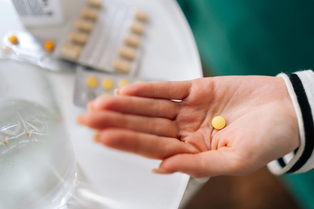 Closeup highangle view of unrecognizable sick young woman holding medicine for flu influenza painkiller vitamin complex oral contraceptives on hands