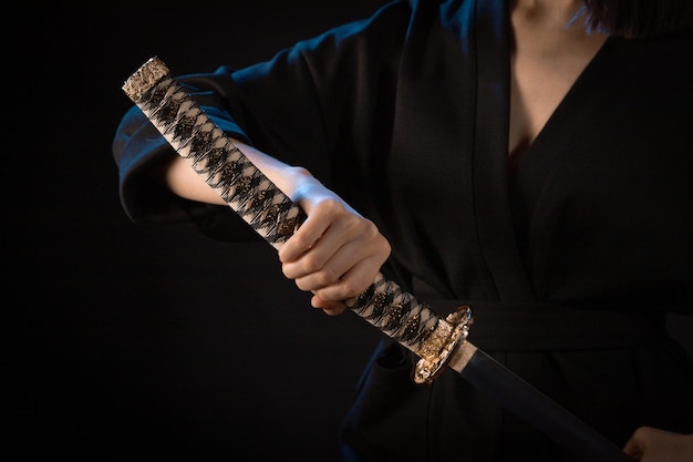 Closeup on the hilt of a Japanese sword in the hand of a woman in a black kimono