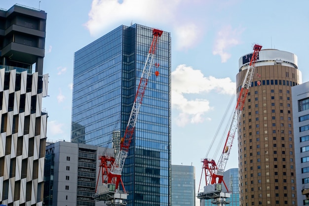 Closeup hoisting cranes working on city landscape view and glass office building with blue sky and silken cloud background.