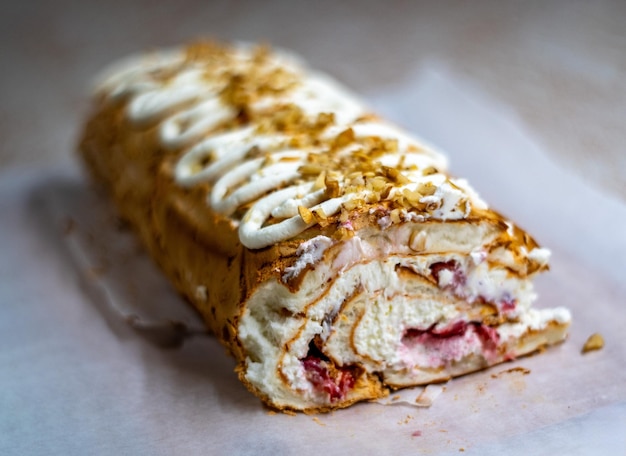 closeup of a homemade meringue roll topped with whipped cream and chopped nuts revealing layers of