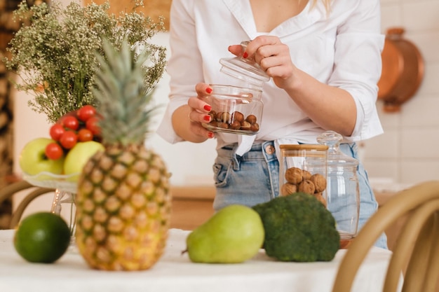 Closeup of the hostess's hands holding nuts in a jar and lying vegetables fruits in the foreground on the kitchen table cooking