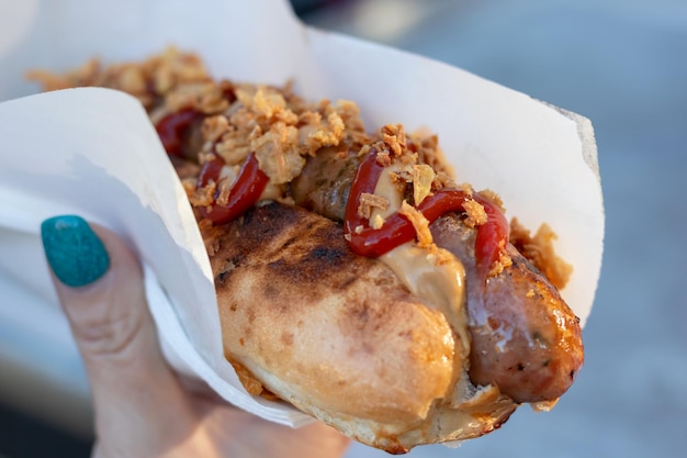 Closeup of a hot dog in a paper napkin with sauce outdoors Selective focus Street food