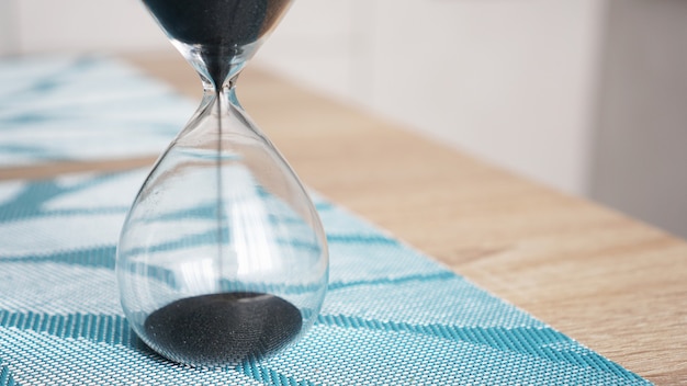 Closeup of hourglass on a white wooden table with defocus kitchen. Concept of time to cook.