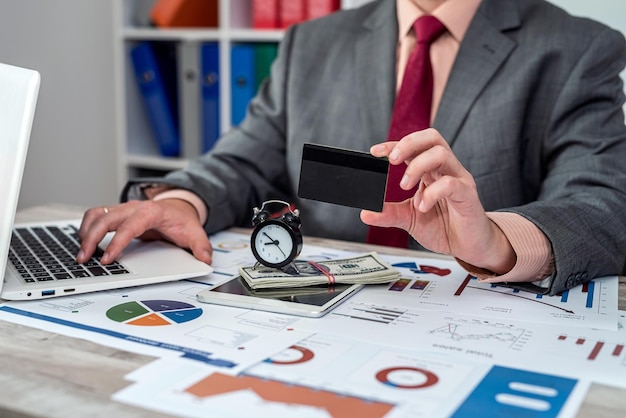 Closeup of human hand of man holding credit card while working on laptop and documents