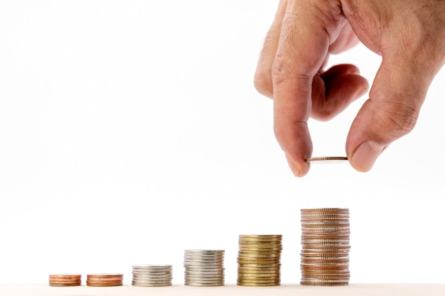 Closeup of human hand putting a coin on a pile of coins over white background, use for business and finance concepts.