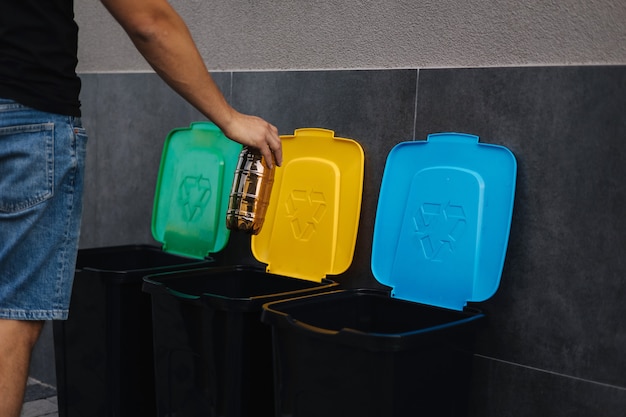 Closeup of human hand throwing empty plastic water bottle in recycling bin tree recycling bins