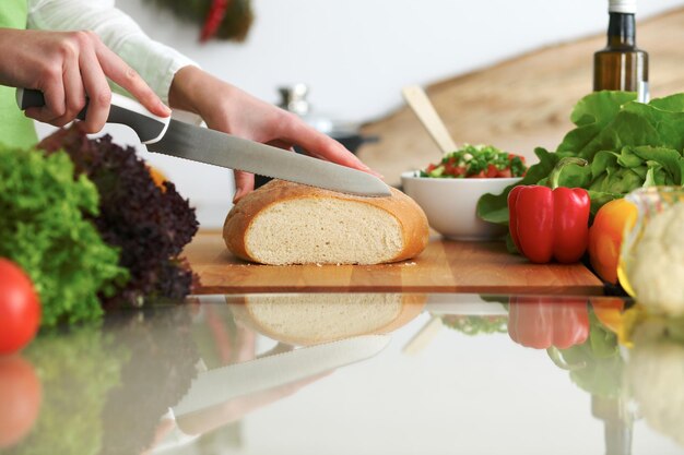 Closeup of human hands cooking in kitchen on the glass table with reflection. Housewife slicing bread.