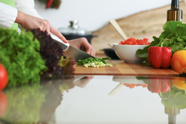 Closeup of human hands cooking vegetables salad in kitchen on the glass table with reflection. Healthy meal and vegetarian concept