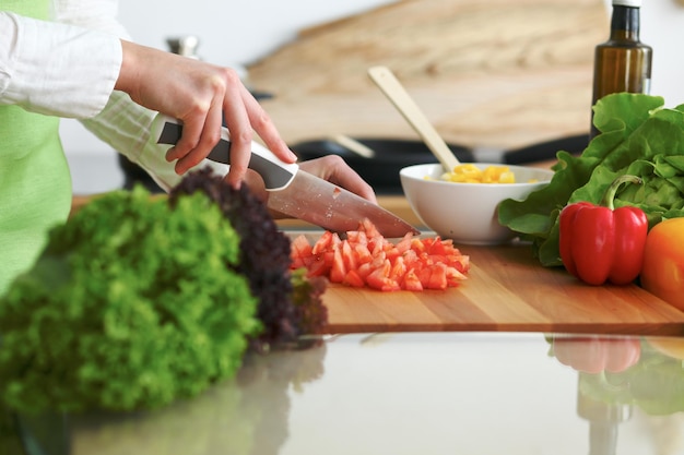 Closeup of human hands cooking vegetables salad in kitchen on the glass table with reflection. Healthy meal and vegetarian concept