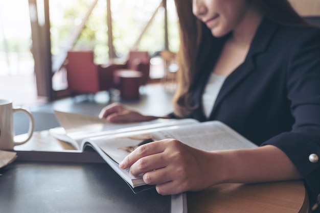 Closeup image of an asian businesswoman reading a book with coffee cup on table in cafe 