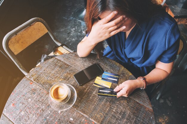 Closeup image of an Asian woman get stressed and broke while holding credit card with mobile phone on the table