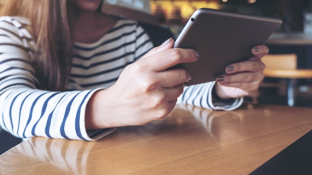 Closeup image of an asian woman holding , looking and using tablet pc in modern cafe