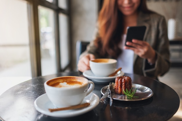 Крупным планом изображение азиатской женщины, держащей и использующей мобильный телефон, попивая кофе в кафе