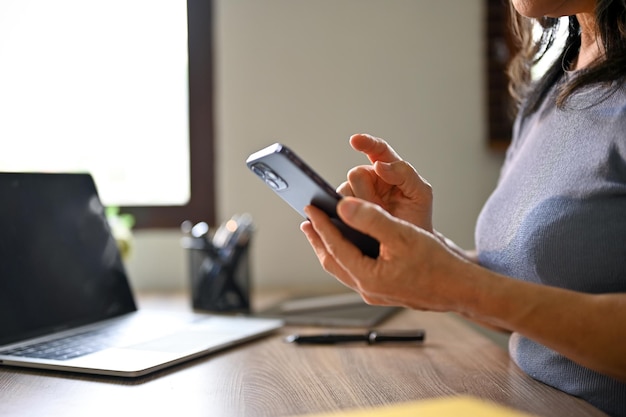 Immagine del primo piano di una femmina asiatica che utilizza il suo smartphone al suo tavolo