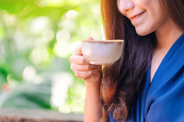 Closeup image of a beautiful asian woman holding and drinking hot coffee in the garden