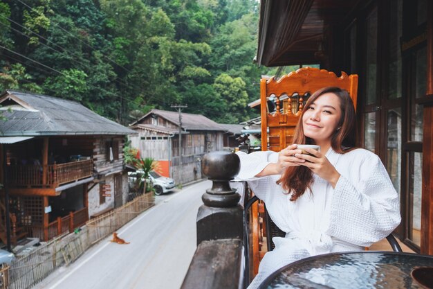 Closeup image of a beautiful asian woman holding and drinking hot coffee in the morning while looking at the old town view