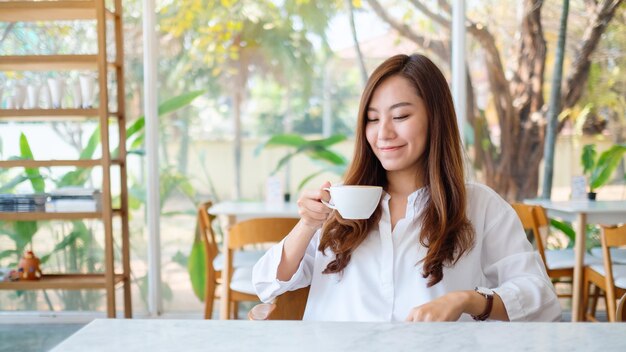 Closeup image of a beautiful asian woman holding and drinking hot coffee with feeling good in cafe