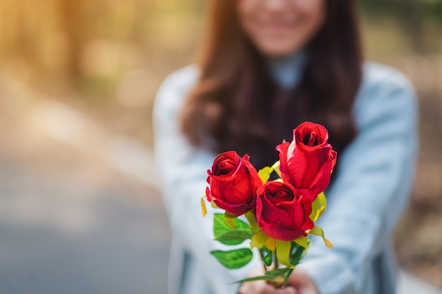 Closeup image of a beautiful asian woman holding and giving red roses flower on Valentine's day