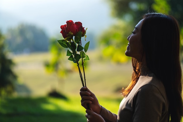 公園で赤いバラの花を保持している美しいアジアの女性のクローズアップ画像